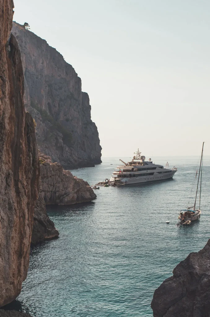 White and Black Boat on Sea Near Brown Rock Formation. Photo by Matias Mango